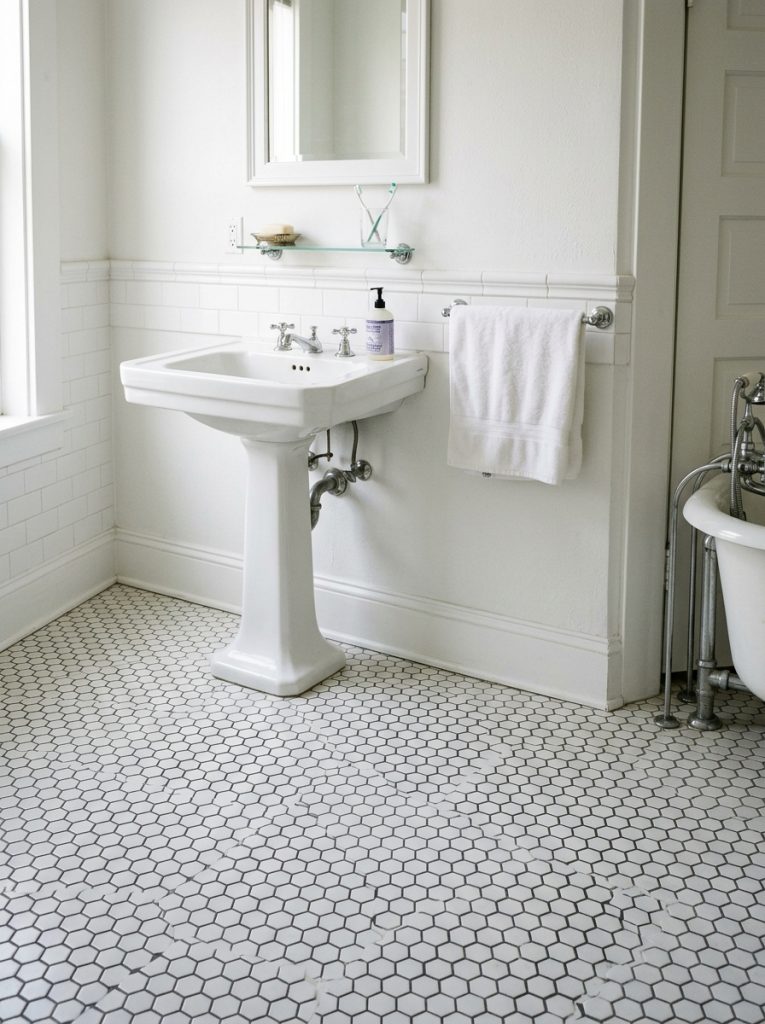 Bathroom floor with classic small white hexagon tiles and dark grey grout with white walls and traditional pedestal sink in timeless vintage aesthetic