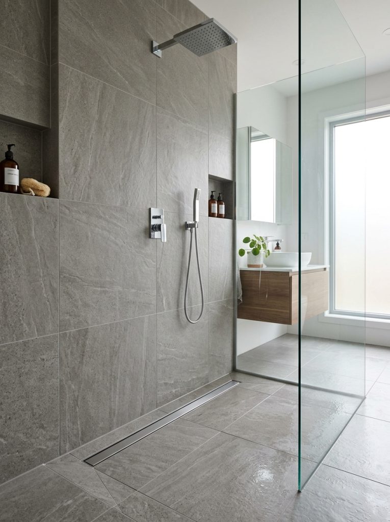 Modern shower with sleek linear drain along wall edge large format stone tiles minimal cuts and clean seamless contemporary look