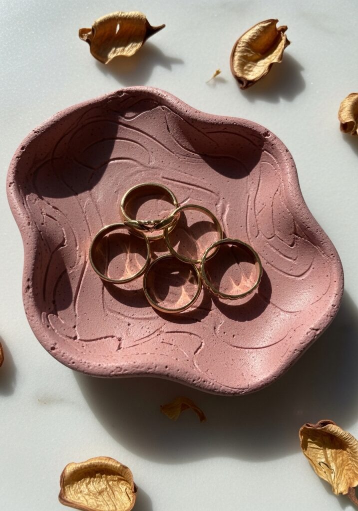 Organic shaped air dry clay ring dish in dusty rose with gold rings on marble surface