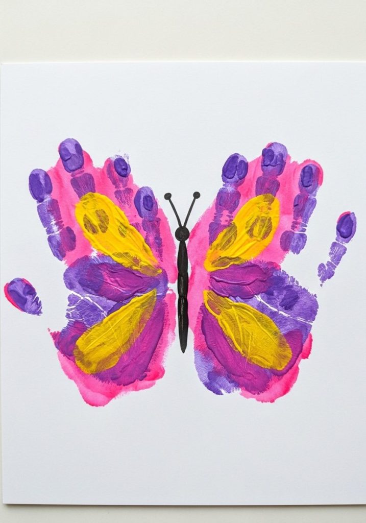 Butterfly handprint mothers day art craft kids two painted handprints mirrored butterfly wings bright pink purple yellow white card painted body antennae vibrant sweet stunning child-made gift