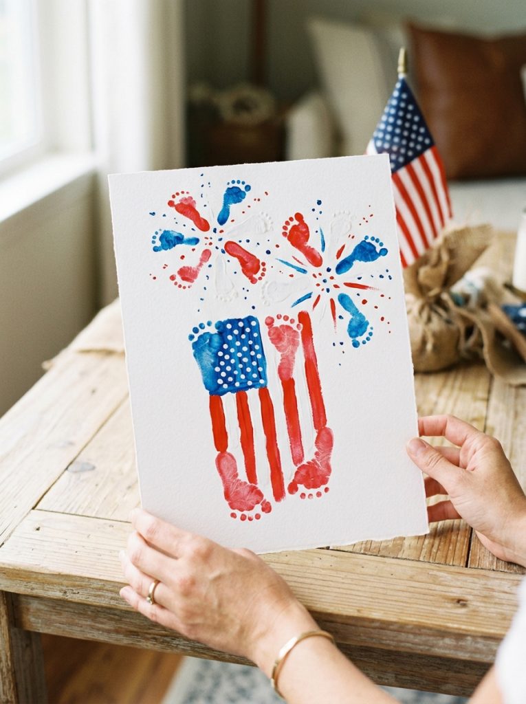 Adorable baby footprint 4th of July craft with tiny red white blue footprints creating patriotic firework design on white paper 