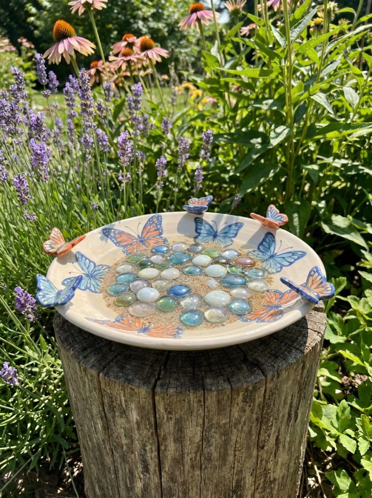 Beautiful decorative ceramic butterfly puddler with butterfly motifs colorful pebbles and water among flowering plants 
