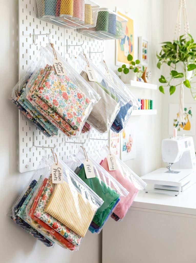 Clear zippered fabric storage bags hanging on wall pegboard with different fabrics visible inside
