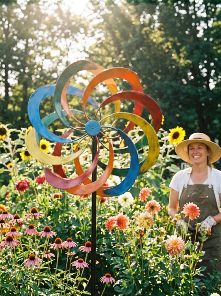 : Colorful metallic garden wind spinner spinning in breeze catching sunlight in bright sunny flower garden