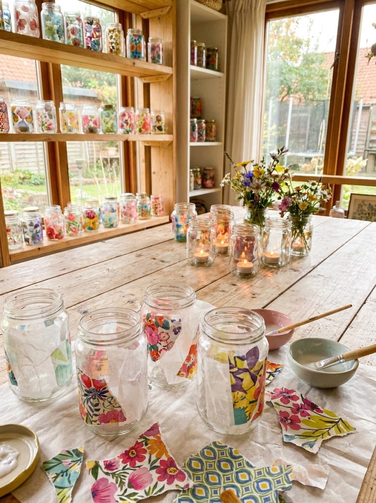 Beautiful decoupage glass jars covered in tissue paper and magazine scraps with candles and flowers inside