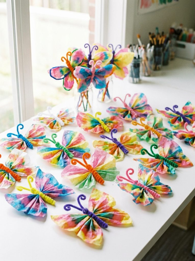 Colorful pipe cleaner butterfly insect crafts in multiple bright colors with tissue paper wings displayed on white surface 