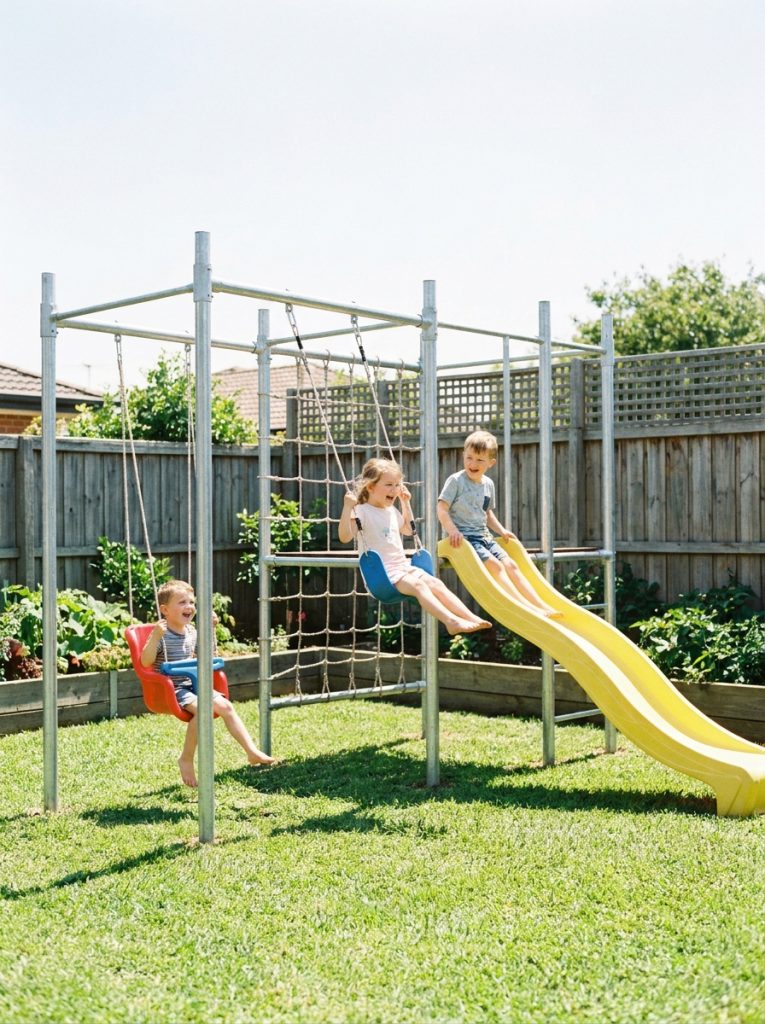 DIY metal frame kids playground with colorful swings and slide in sunny backyard