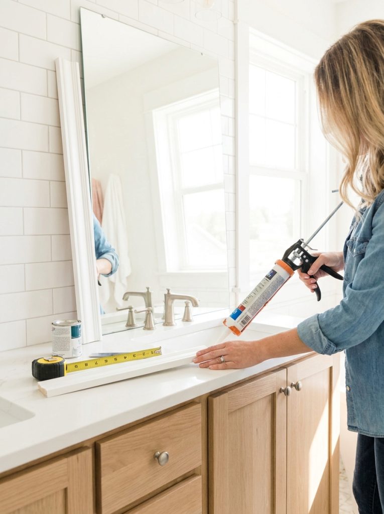  DIY bathroom vanity mirror frame with white painted wood molding applied over builder grade frameless mirror
