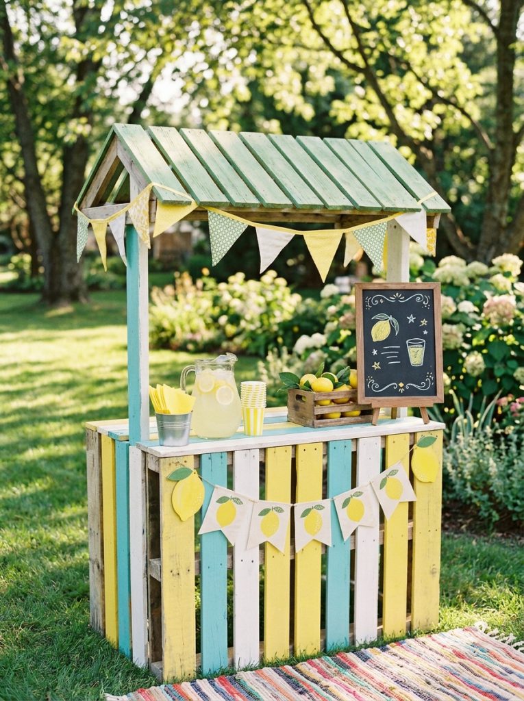 Charming pallet lemonade stand DIY sized for kids with bright painted colors lemon decorations and handmade menu sign outdoors