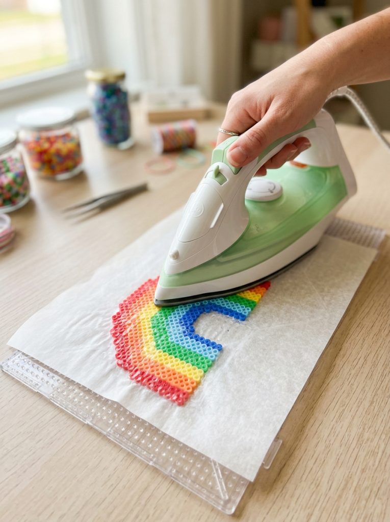 Perler bead ironing paper positioned over colorful bead design on pegboard showing essential fusing step transforming loose beads to pattern 