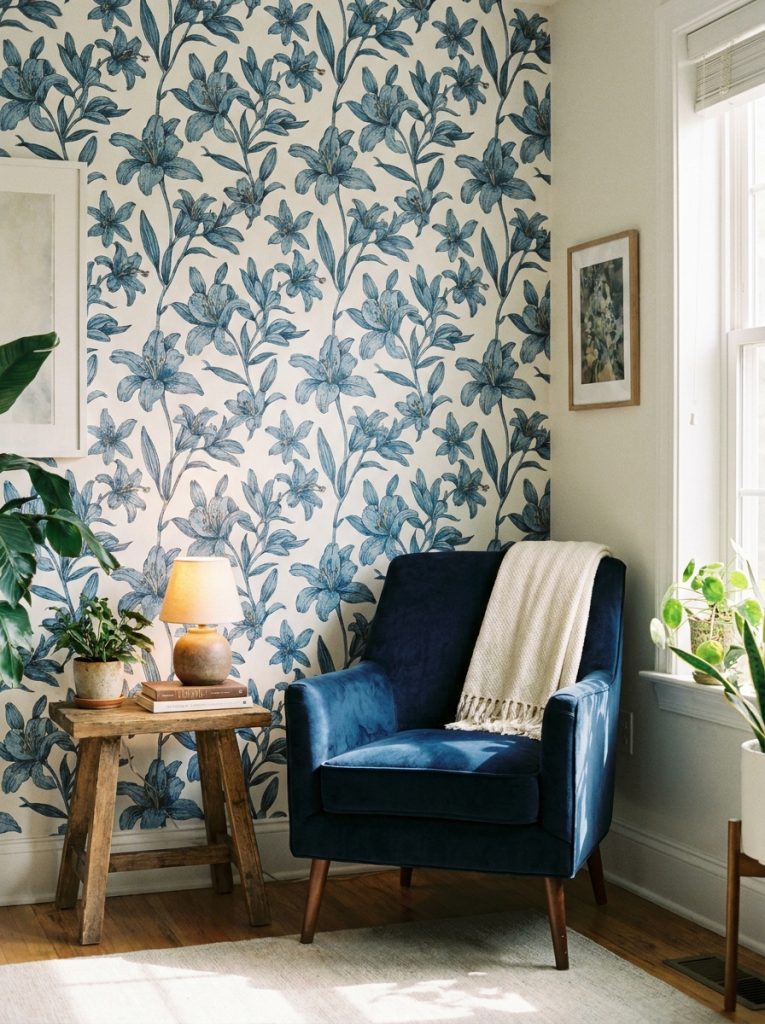 Beautiful blue lilies wallpaper room with navy armchair wooden side table and soft lamp light.